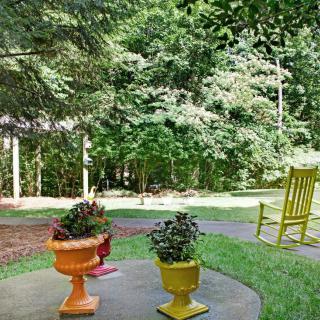 A tranquil outdoor patio with colorful potted plants and a yellow rocking chair overlooking lush greenery.