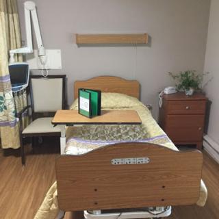 A view of a hospital patient room featuring a bed, medical equipment, and a bedside table.