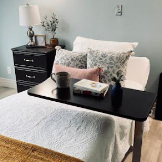 A cozy bedroom setup featuring a neatly made bed, decorative pillows, a bedside table with a lamp and books, creating a tranquil atmosphere.