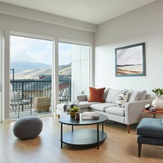 A modern living room with a view of the mountains through large sliding glass doors, featuring neutral colors and cozy furnishings.