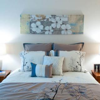 A cozy bedroom with decorative pillows, artwork above the bed, and soft lighting from bedside lamps.