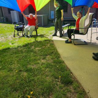 Seniors enjoy a lively outdoor game with colorful parachutes, fostering fun and community engagement.