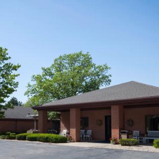 A single-story brick building with a driveway, surrounded by trees under a clear blue sky.