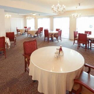 An elegant dining room with round tables and red chairs, featuring chandeliers overhead.