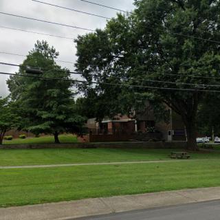 A suburban house surrounded by trees and a well-maintained lawn, under an overcast sky.