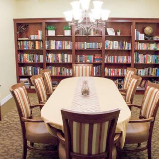 A cozy library room with a long table, surrounded by bookshelves filled with books.