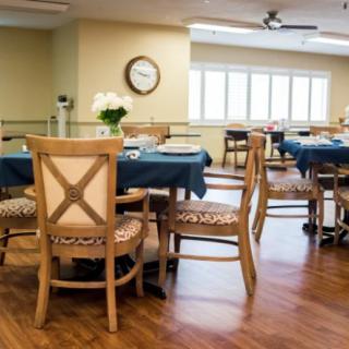 A well-lit dining area with wooden chairs and tables, set for a meal.