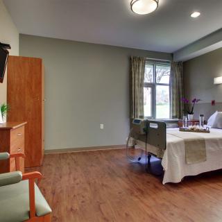 A hospital room with a bed, chair, television, and large window with curtains.