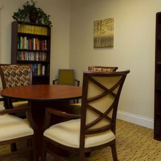 A cozy meeting room with a wooden round table surrounded by chairs, and bookshelves filled with books.