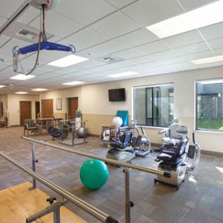 A spacious physical therapy gym equipped with various exercise machines and a blue exercise ball, designed for rehabilitation and fitness activities.
