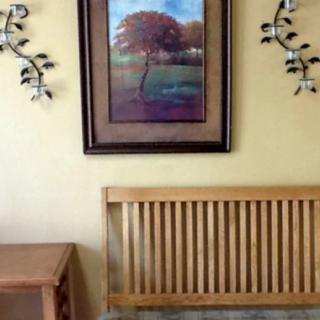 A cozy interior with a framed landscape painting, decorative wall accents, a wooden bench, and a side table.