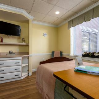A cozy bedroom with a single bed, a wall-mounted television, and a window providing natural light.