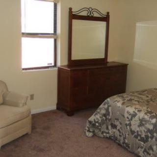 A simple bedroom with a bed, dresser, mirror, chair, and window.