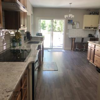 A modern kitchen with wooden cabinets, a sleek countertop, and hardwood floors leading to a dining area with natural light through sliding doors.