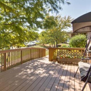 A sunny wooden deck with a swing bench, surrounded by trees.