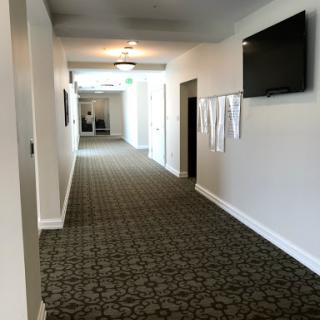 A well-lit hallway with patterned carpet and a wall-mounted television.
