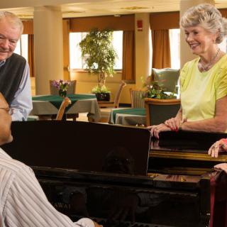A group of seniors gathered around a piano enjoying music together.