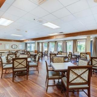 A spacious dining area with multiple tables and chairs, featuring large windows and a wooden floor.