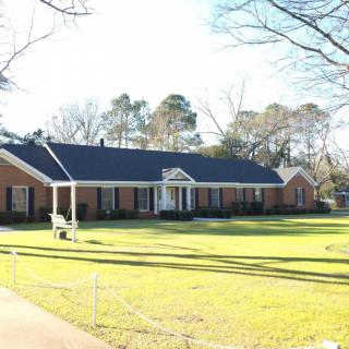 A suburban brick house with a well-maintained lawn and surrounding trees.