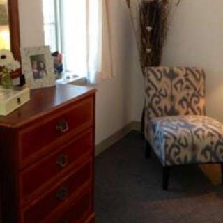 A cozy bedroom corner featuring a patterned chair, dresser, and decorative items by the window.