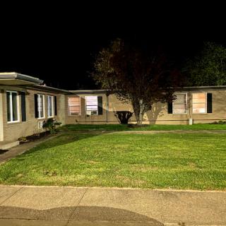 A quiet residential building illuminated at night, surrounded by well-maintained grass.