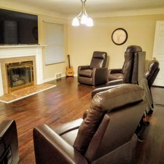 A cozy living room with leather recliners arranged around a fireplace and television, featuring warm wood flooring and a guitar in the corner.