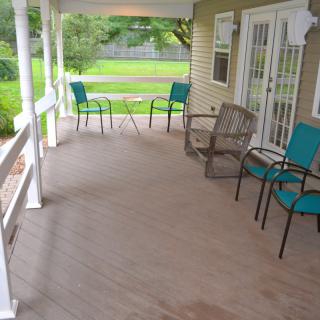 A cozy covered porch with several chairs and a table overlooking a green yard.