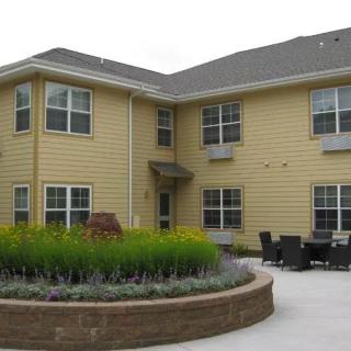 A two-story yellow house with a landscaped garden and patio area.