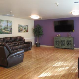 A modern living room with a purple accent wall, leather sofas, and a mounted television.