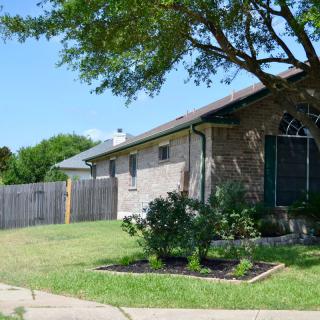 A suburban brick house with a green lawn and trees in the front yard.