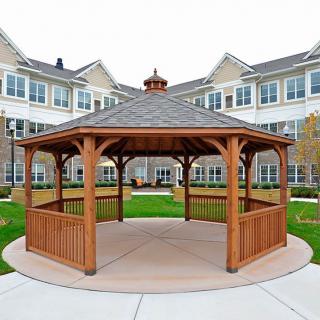 A wooden gazebo situated in the garden area of a residential building.