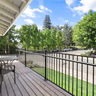 A scenic balcony with outdoor seating overlooks a lush, tree-lined street.