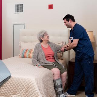 A caregiver assists an elderly person in a bedroom setting.