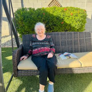 An elderly woman enjoying a sunny day on a swing in her backyard.