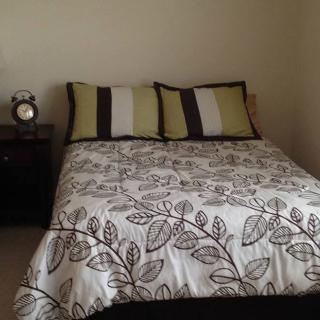 A neatly arranged bed with patterned bedding and decorative pillows, accompanied by a nightstand with an alarm clock.
