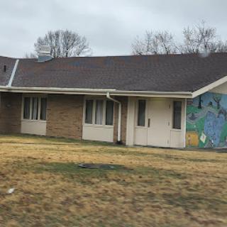A residential building featuring a colorful mural on one side, surrounded by sparse grass in an overcast setting.