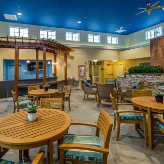 A spacious indoor seating area with wooden tables and chairs, decorated with small plants under a vibrant blue ceiling.
