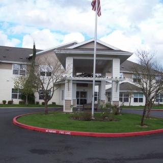 A large building with an American flag at the entrance, featuring a circular driveway and landscaped greenery.