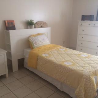 A minimalist bedroom with a single bed featuring yellow bedding, accompanied by white furniture including a nightstand and dresser.