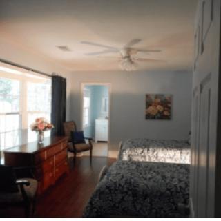 A cozy bedroom with natural light, featuring a bed, dresser, and artwork on the wall.