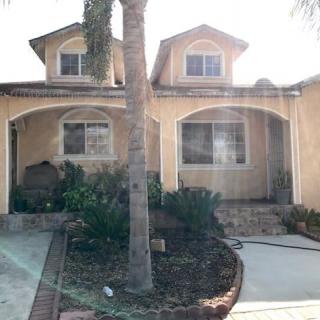 A two-story suburban house with a driveway and a palm tree in the front yard.