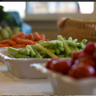 A close-up of fresh vegetables including carrots, celery, and cherry tomatoes arranged on a table.