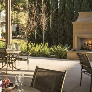 A cozy outdoor patio with dining tables and a fireplace surrounded by trees.