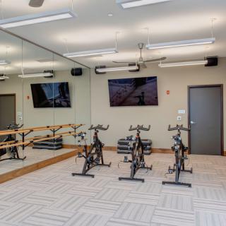 A modern fitness room equipped with exercise bikes, large mirrors, and a television.