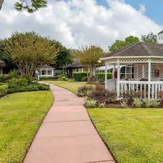 A peaceful garden featuring a walkway leading to a gazebo, surrounded by lush greenery and trees.