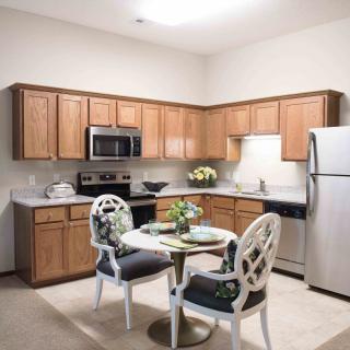 A modern kitchen with wooden cabinets, stainless steel appliances, and a small dining table with two chairs.