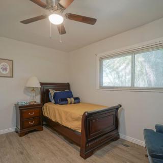 A cozy bedroom with a single bed, wooden furniture, and a ceiling fan.