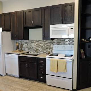 A modern kitchen featuring dark cabinets, a white refrigerator, microwave, oven with stove, dishwasher, and decorative backsplash.