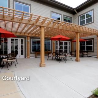 A spacious outdoor courtyard with a pergola, tables, and red umbrellas.
