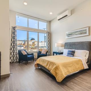 A modern bedroom with a large window, featuring a stylish bed, two chairs, and abundant natural light.